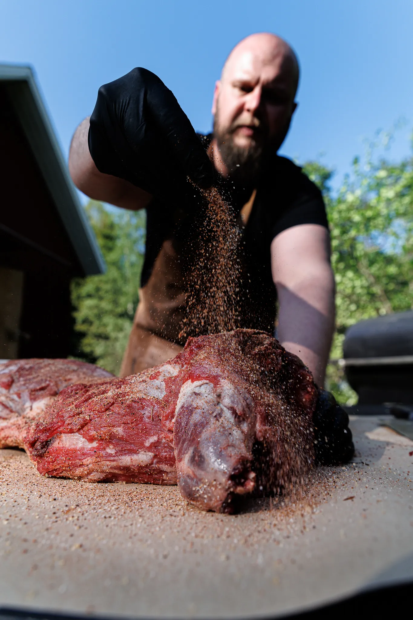Mies maustaa isoa raakaa lihaa ulkona aurinkoisena päivänä.